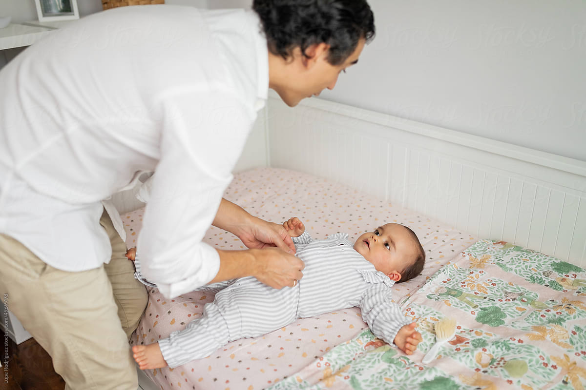 young father dressing his baby in bedroom