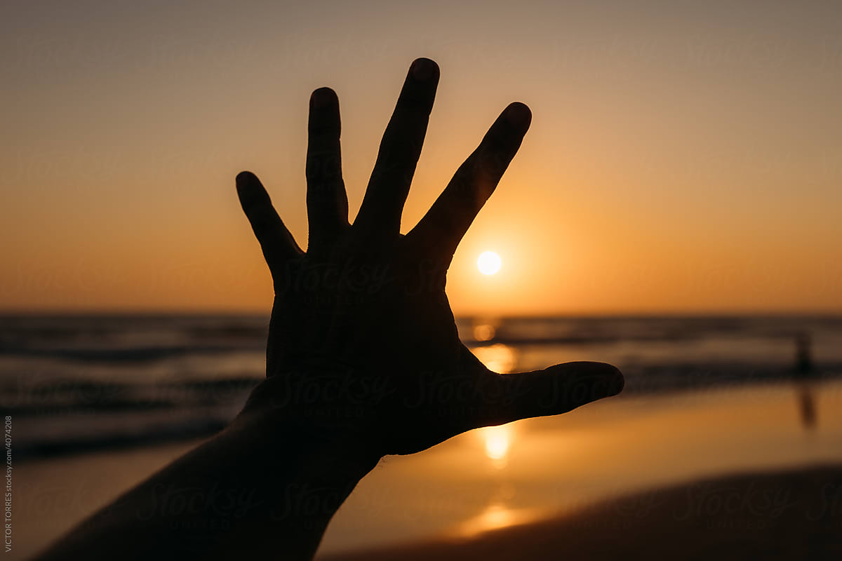 Person outstretching hand against sunset sky