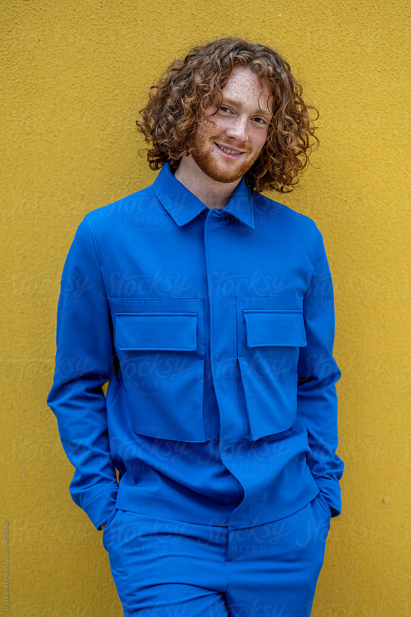 Happy redhead male in blue clothes against yellow wall