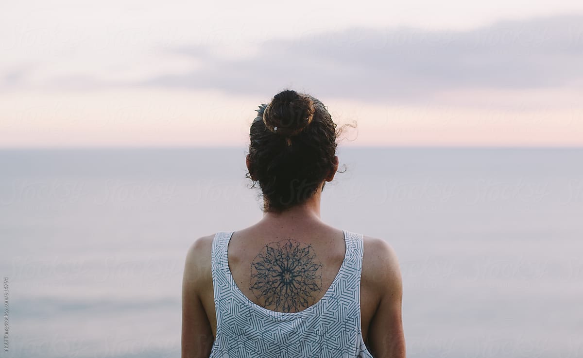 Young man with hair bun and mandala tattoo at the ocean sunset view point