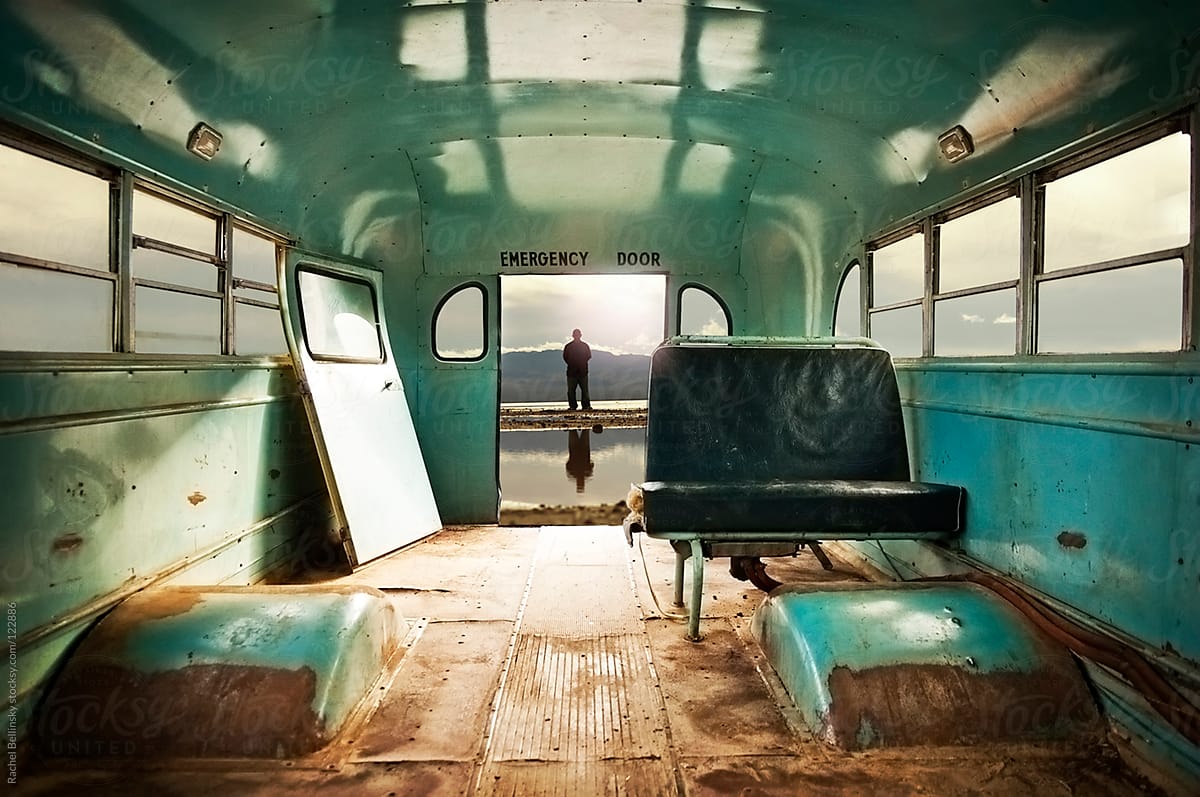 A man in a distant watery horizon seen through the emergency exit of a rusty abandoned bus