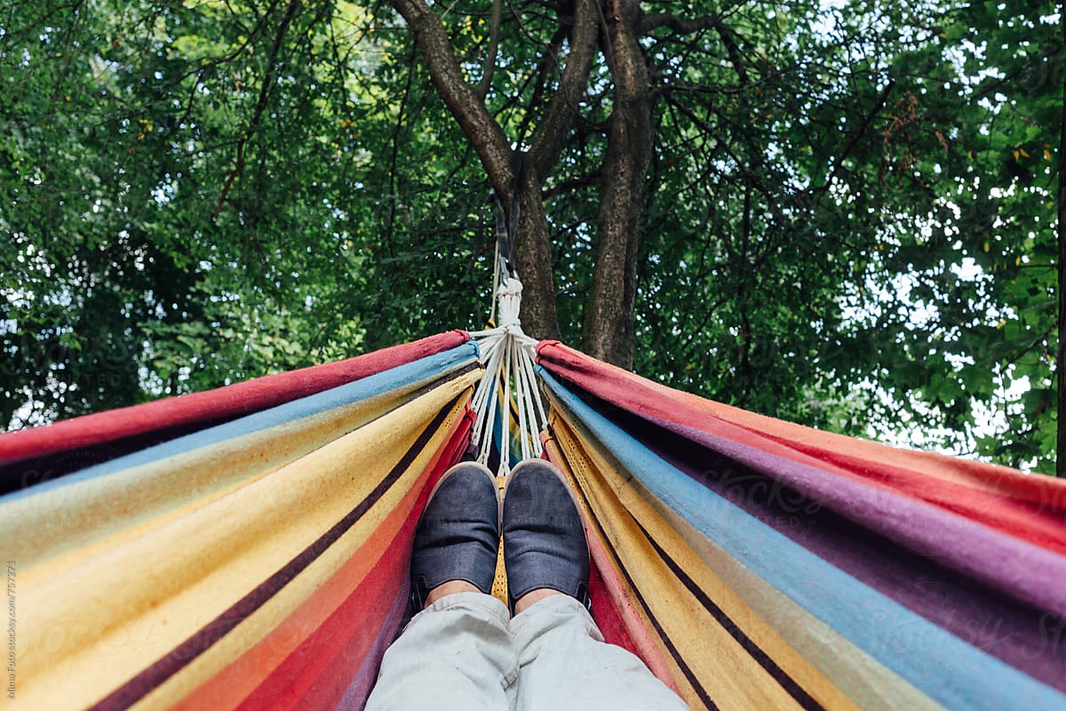 Man in blue sneakers lying in colorful hammock, top view, personal perspective, footsie.