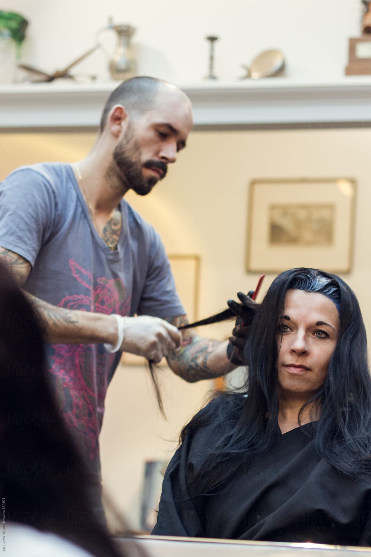 Woman is getting her hair colored by a  tattooed hairdresser