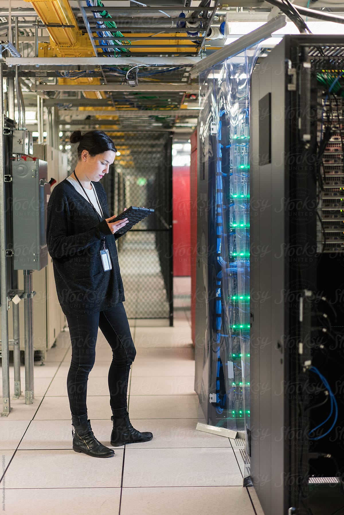 Young woman in a server room looks down at her digital tablet