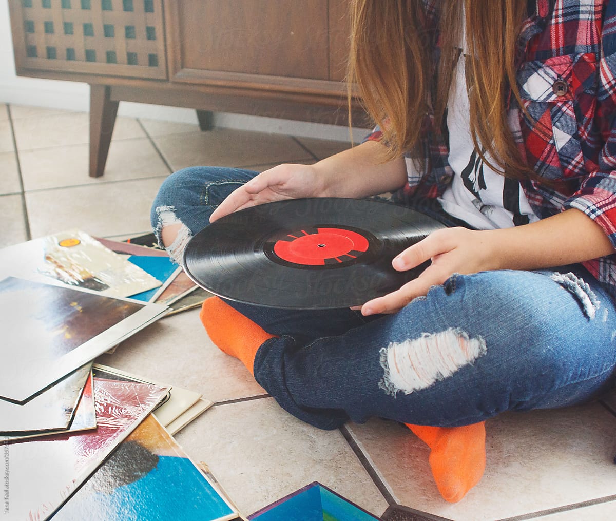 Teen holds 33 LP vinyl record while sitting on floor with albums