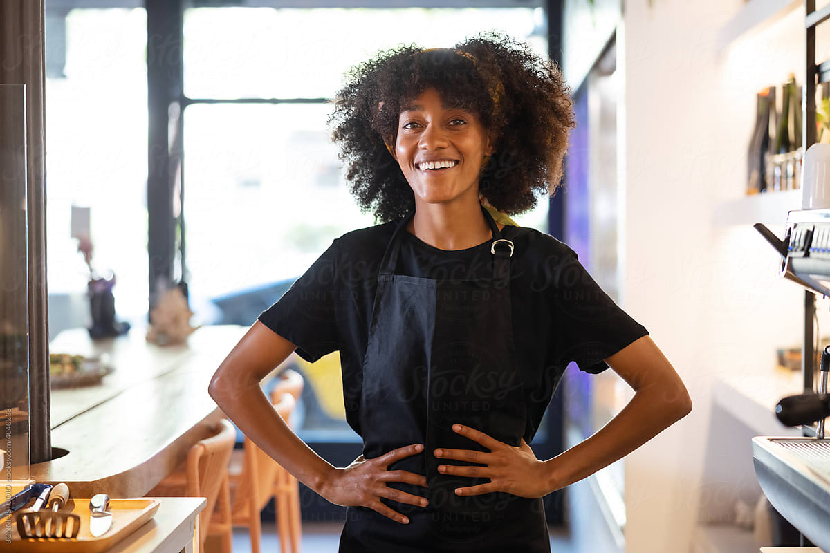 Smiling black female barista in apron standing in cafe
