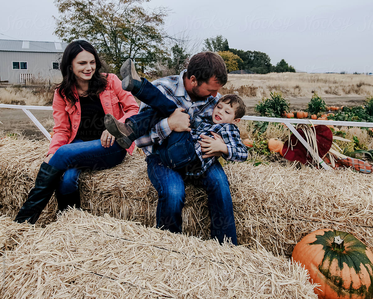 family rides in hay wagon with pumpkins