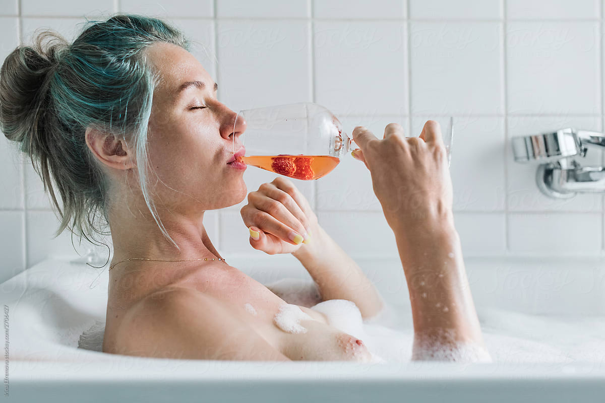 Blue haired woman enjoying a drink in a bathtub