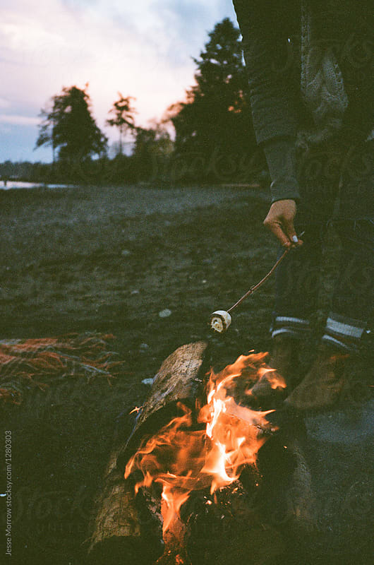 young woman roasting marshmallow over fire on beach