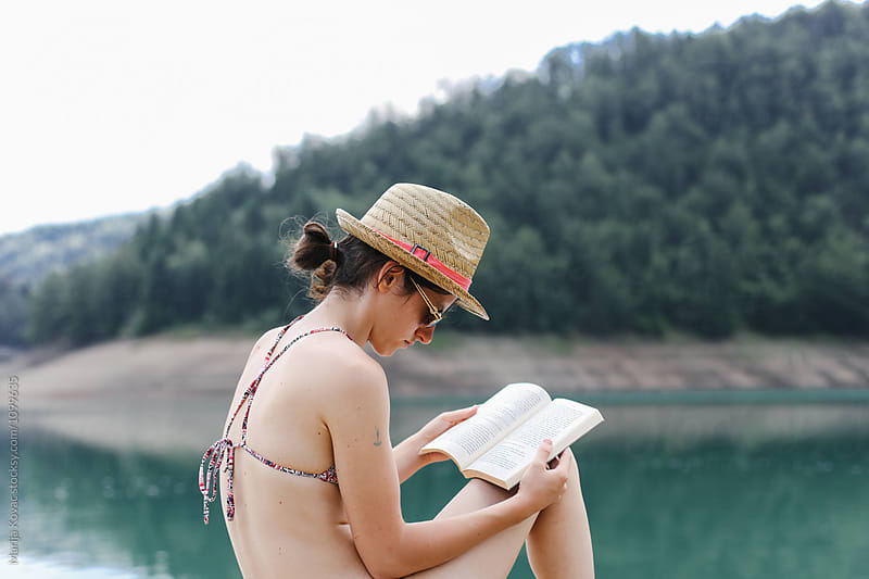 Young woman reading a book, near the lake