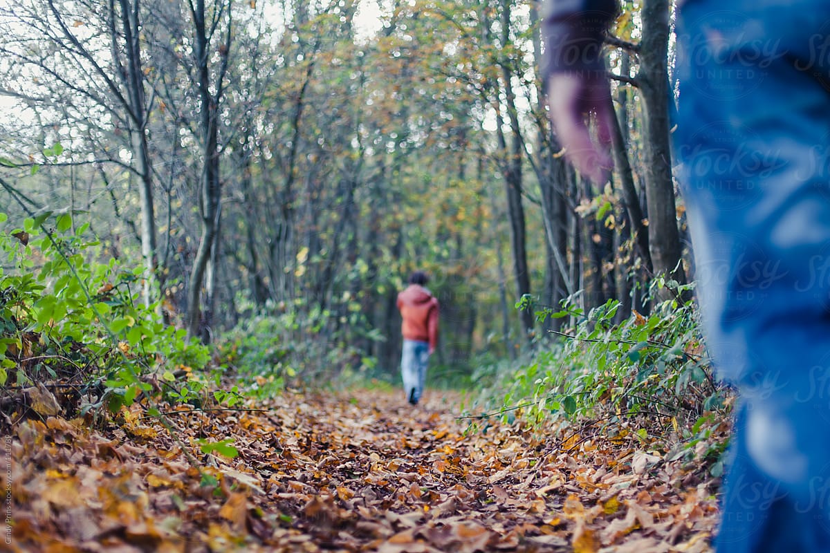 Teenager in orange jacket from the back walking in the woods with someone watching