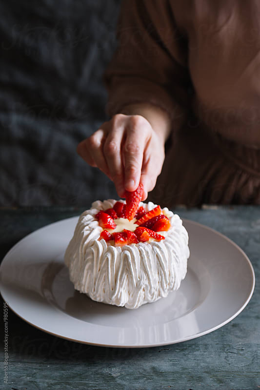 Woman decorating pavlova cake with strawberry