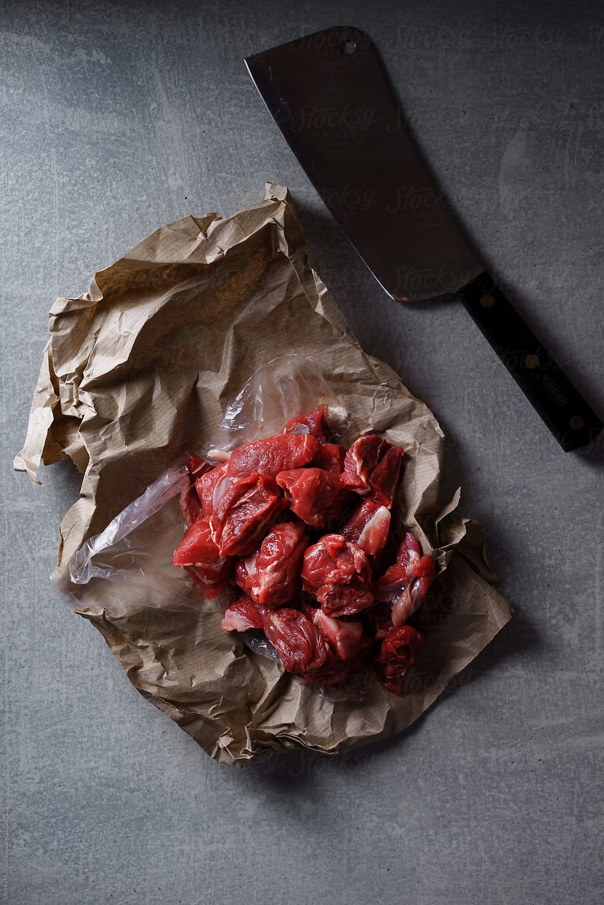 Fresh diced beef in butchers paper and a meat cleaver on stone background.