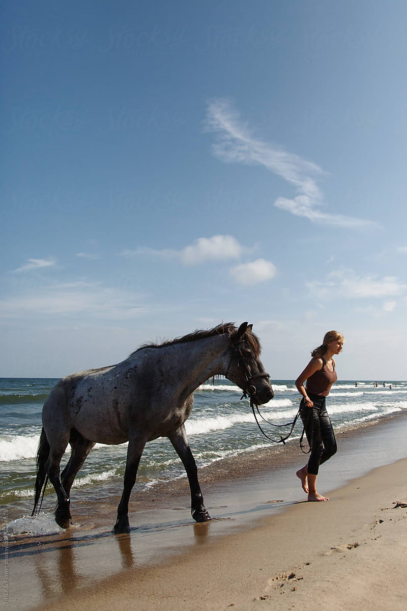 Barefoot woman with horse walking near sea