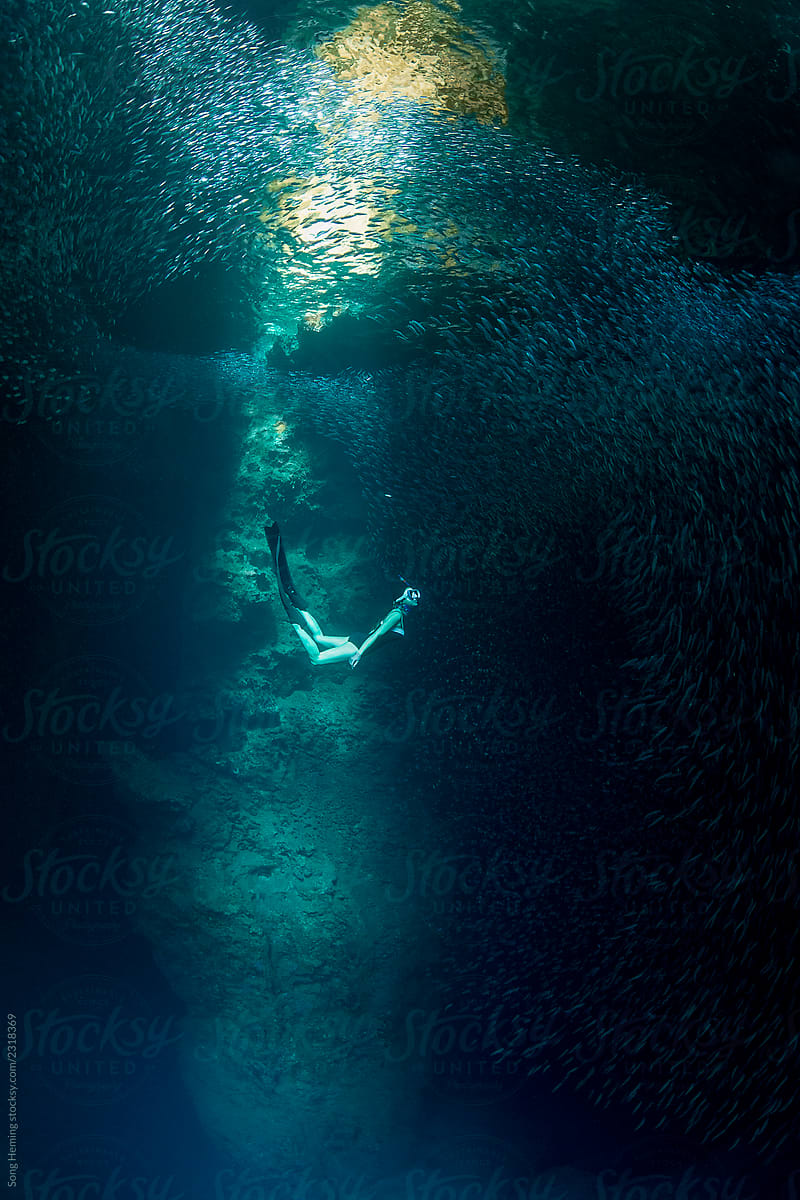 Female free diver with schooling fish underwater in the cavern with light