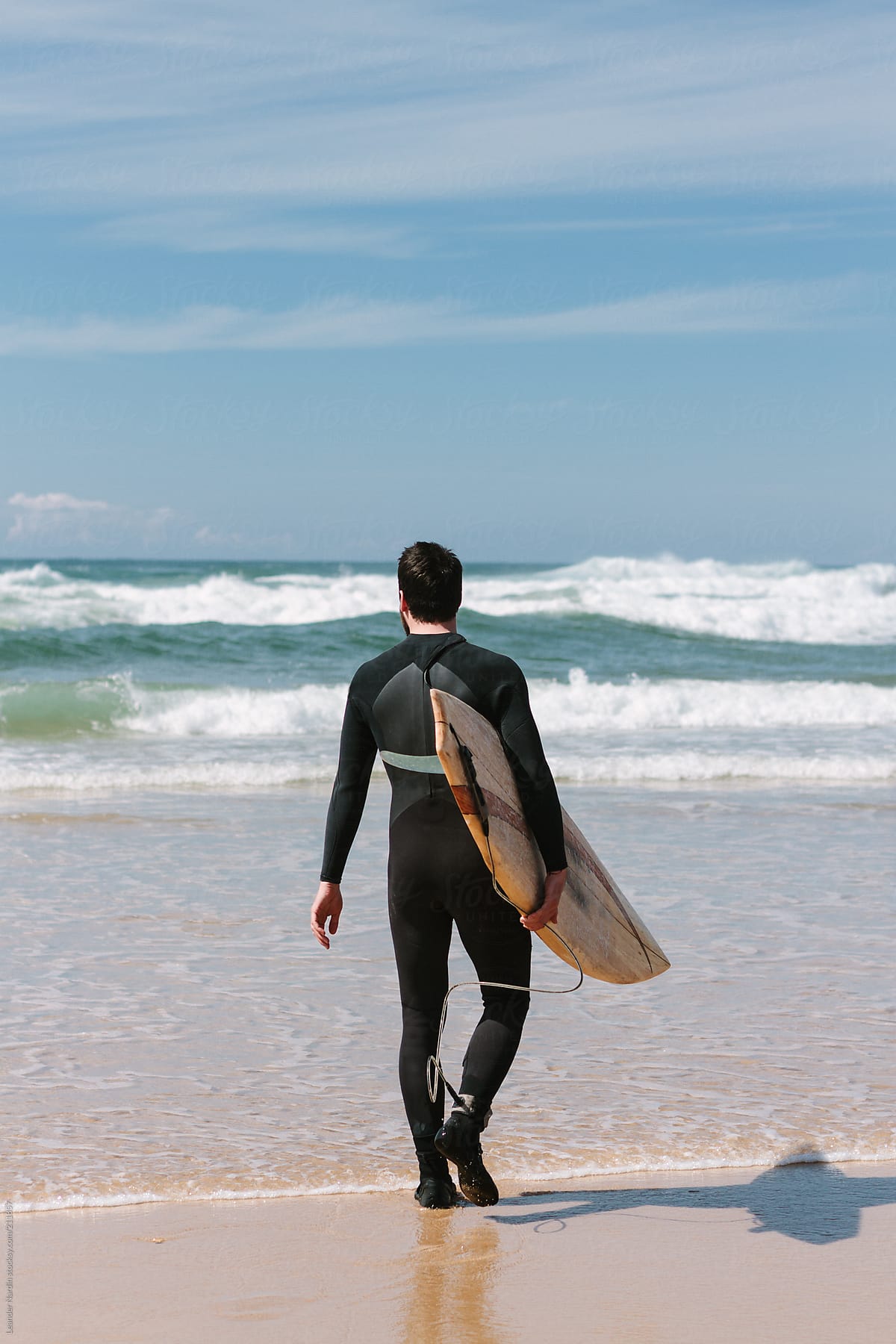 surfer walking into ocean with his surfboard