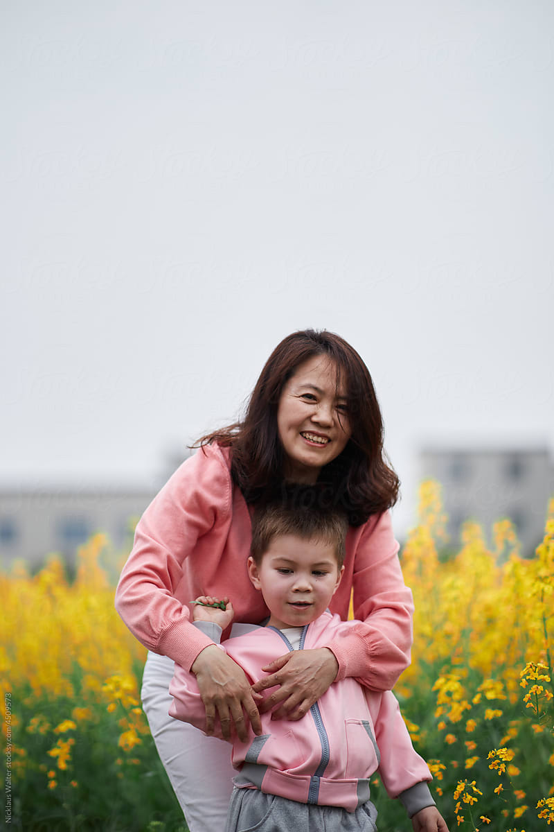 Beautiful Asian Grandmother Smiles And Holds Her Grandson At A Park.
