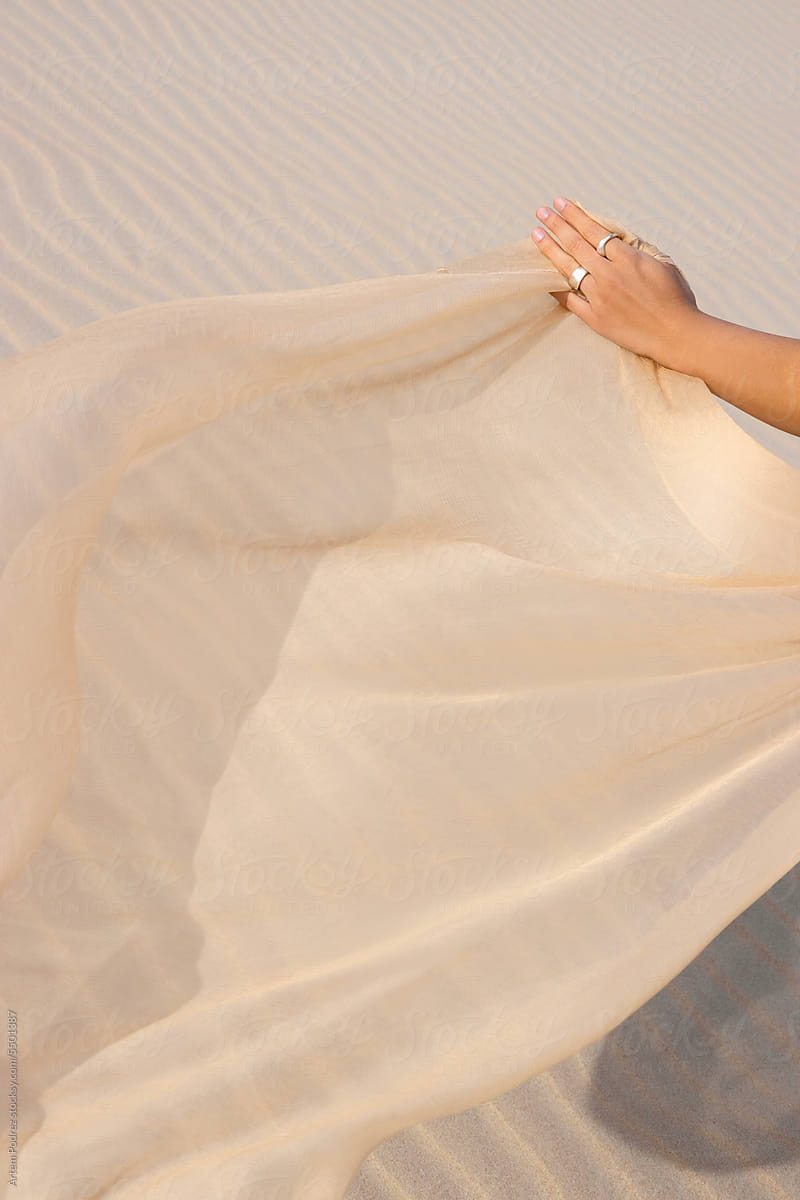 A woman\'s hands flying a silk fabric in the wind.