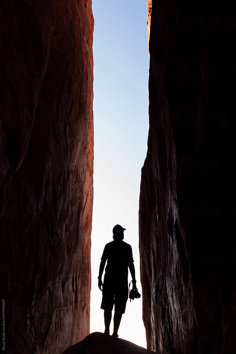 A man stands below two sandstones walls in Arches National Park