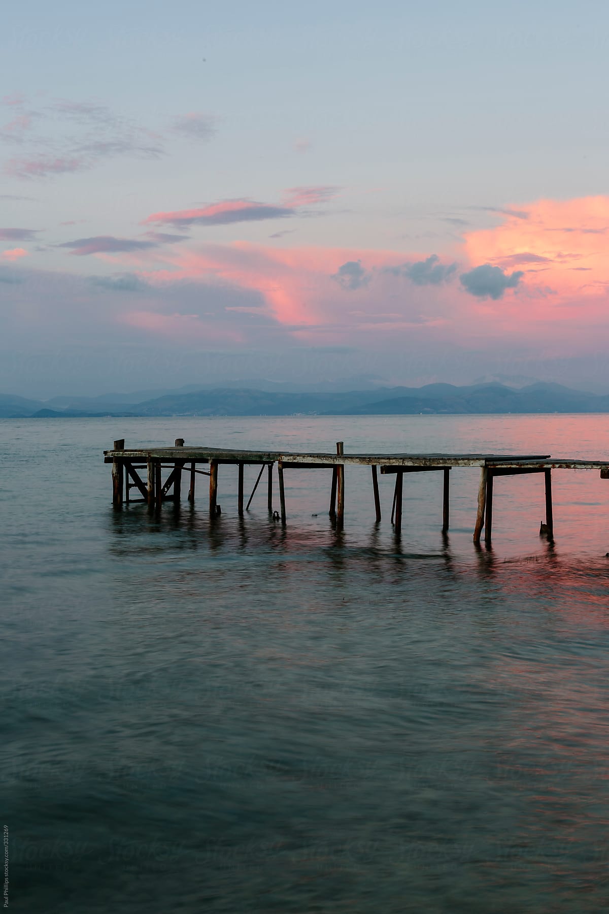Small fishing pier in a calm sea at dawn. Pink light reflected in the sea and clouds