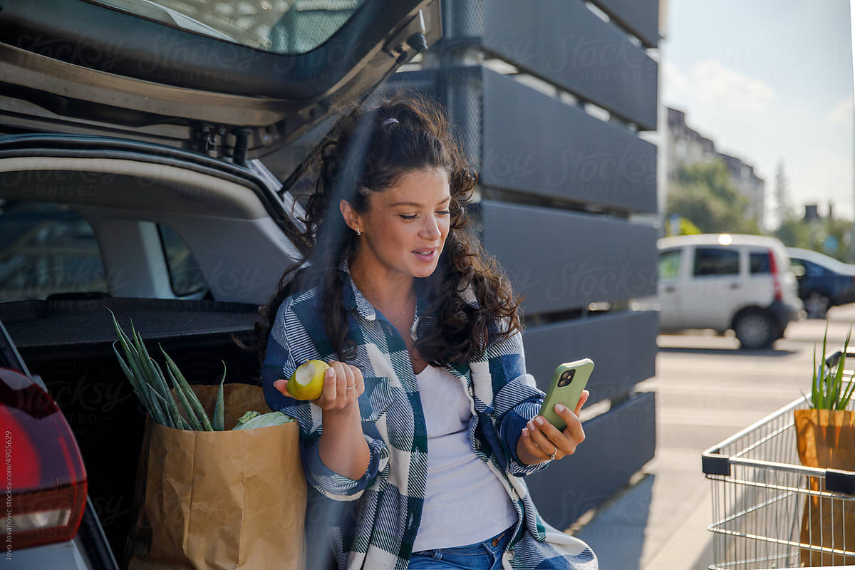 Pregnant woman stopping to eat while loading groceries in car