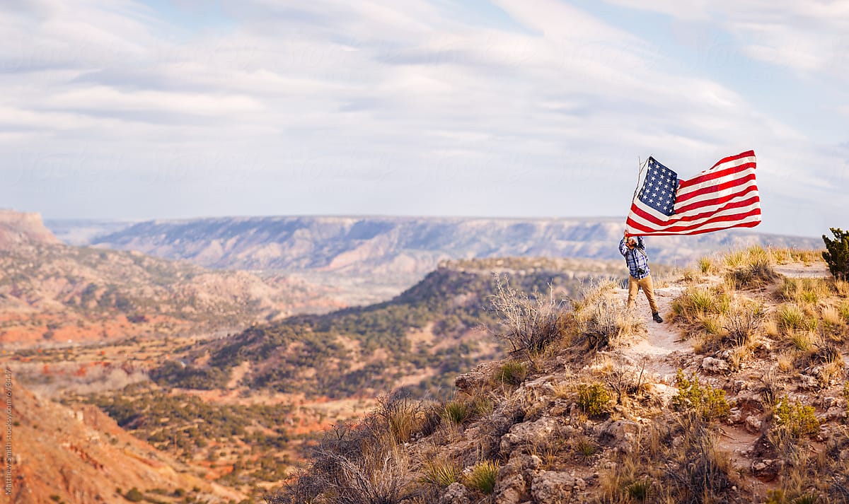 Man Proudly Waving An American Flag On A Canyon Overlook
