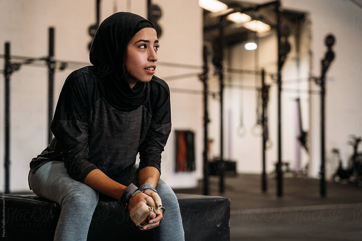 Confident Muslim sportswoman in headscarf sitting in gym