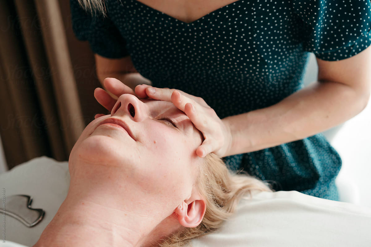 Female hands massaging face of relaxing woman.