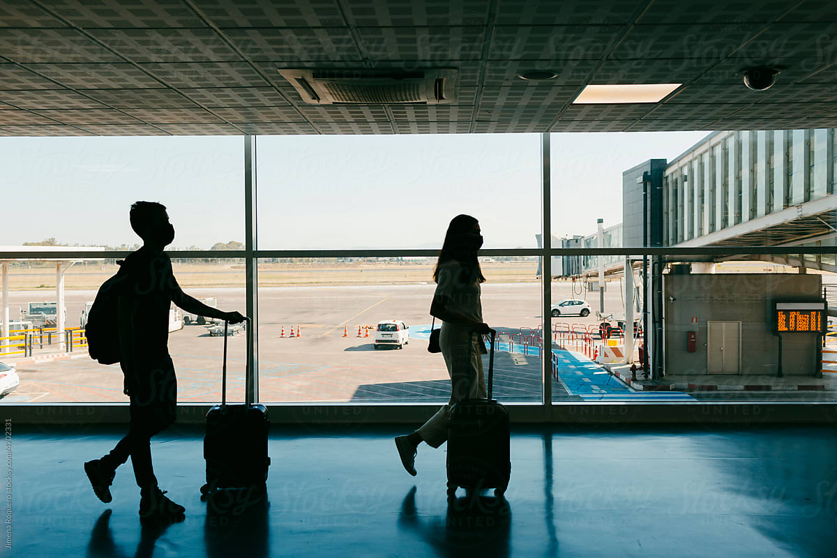 Silhouette of travelers with carry-on luggage on airport terminal