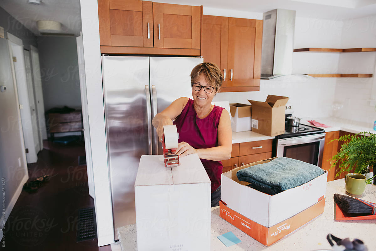 Smiling mature woman packing up kitchen box with tape.