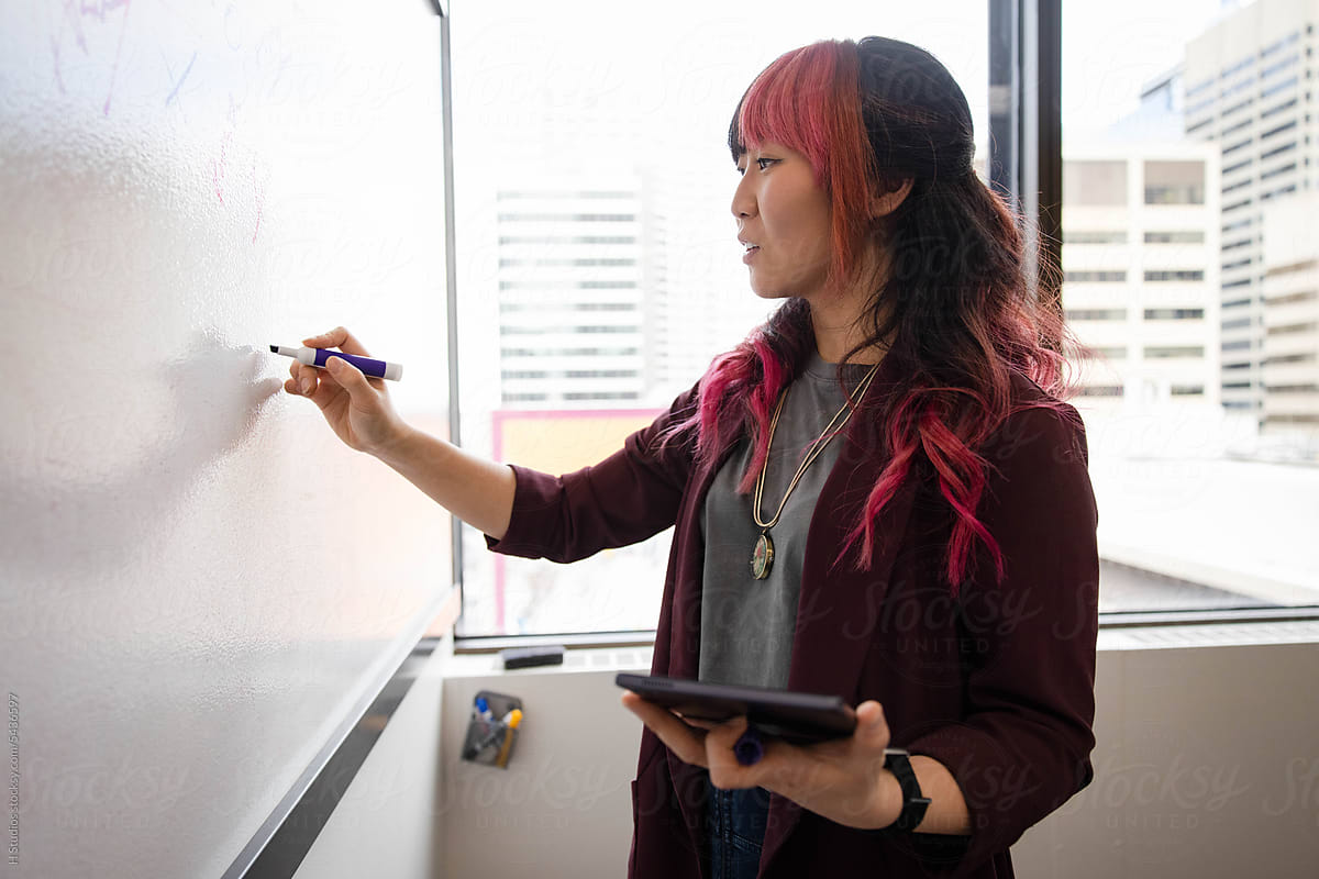 Businesswoman with pink hair planning at whiteboard in office