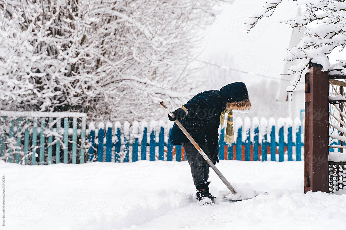 Kid Boy clearing snowy path in a suburban or countryside house yard