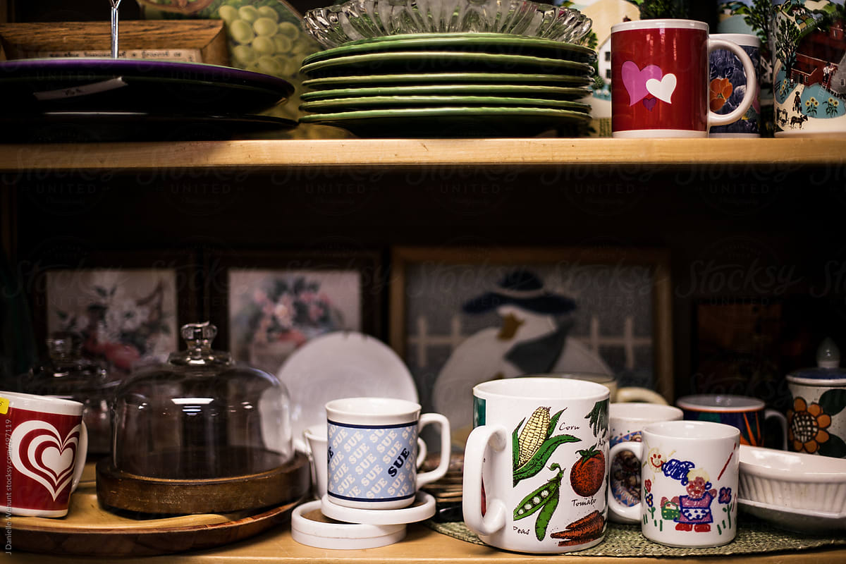 mugs, plates, knick knacks on a shelf in a second hand store