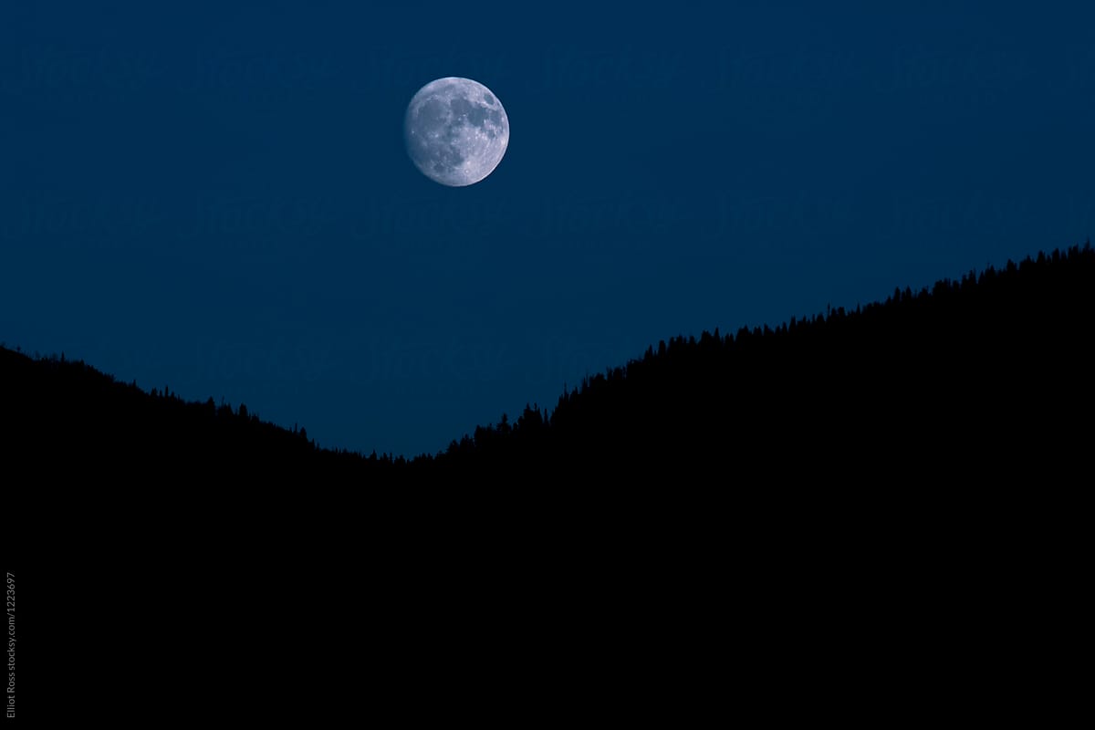 A full moon rises over a mountain