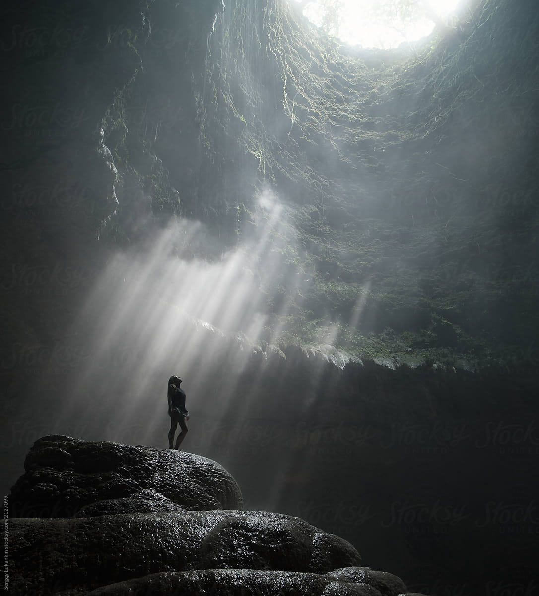 Girl stands under the rays of light in a deep cave Jomblang Cave. Java, Indonesia