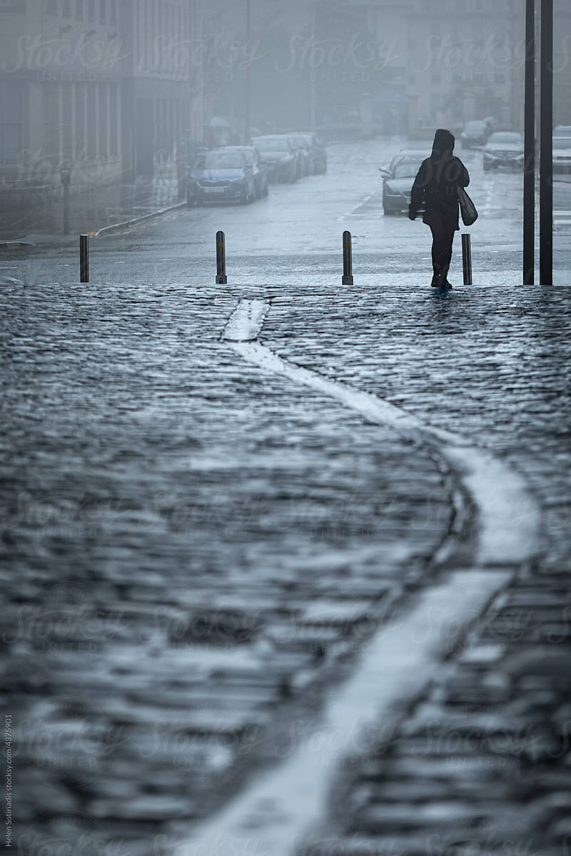 Silhouette Walks exits a Cobblestone Pedestrian Street in the Rain