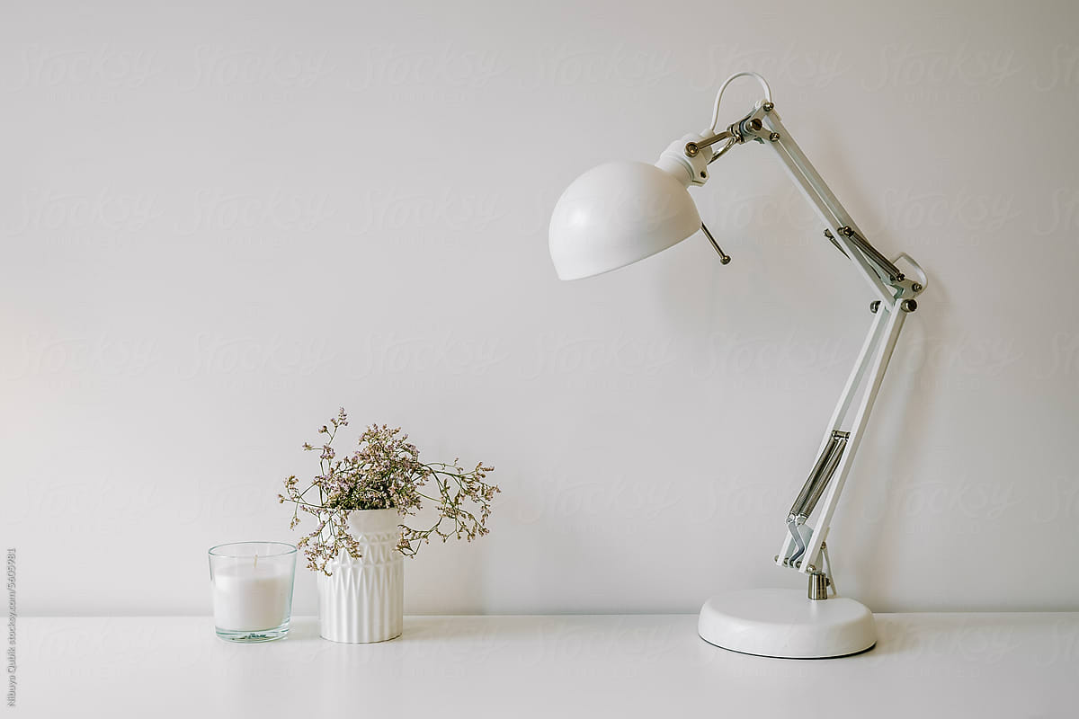 White table detail with white metal floor lamp, candle and houseplant
