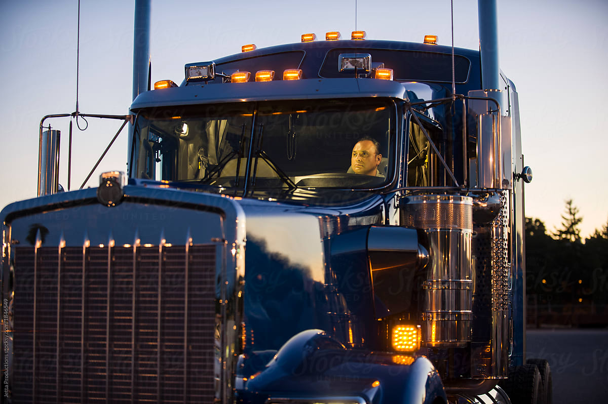 Hispanic truck driver in cab of truck at sunset.