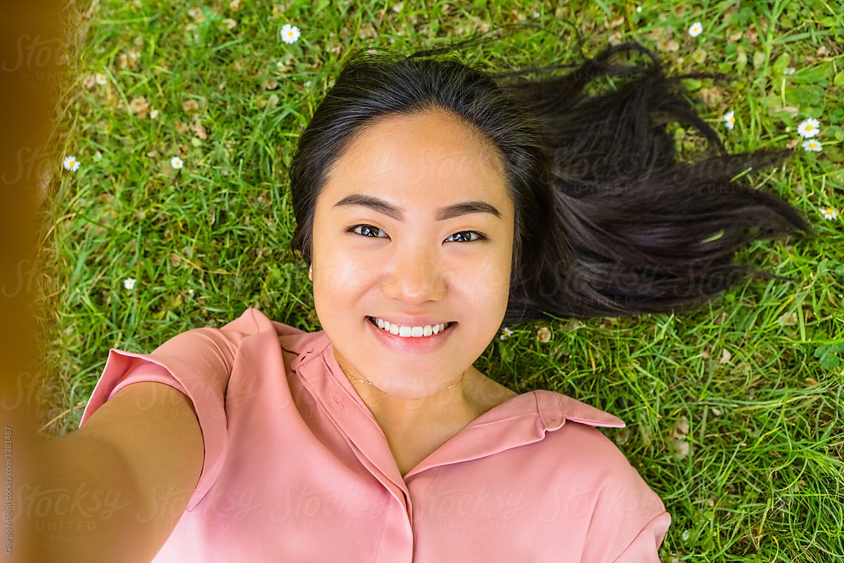 Young Filipino Woman Taking a Selfie while Lying Down on Grass by Giorgio M...