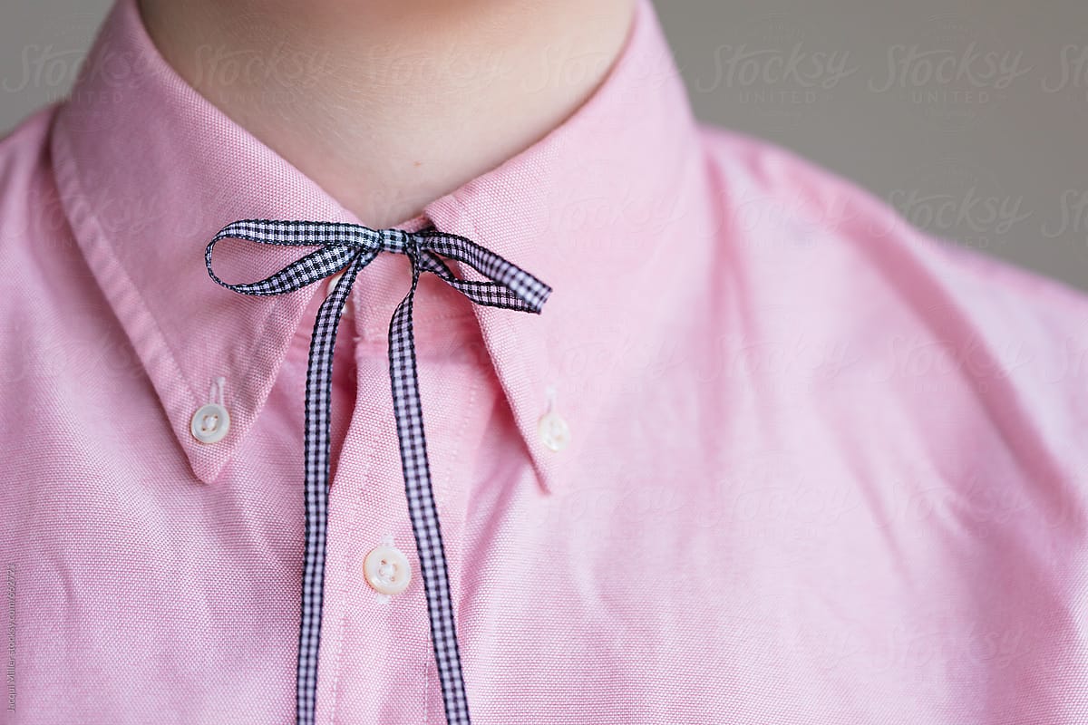 Close up of girls neck. She\'s wearing a collared pink shirt with a ribbon tied at the neck
