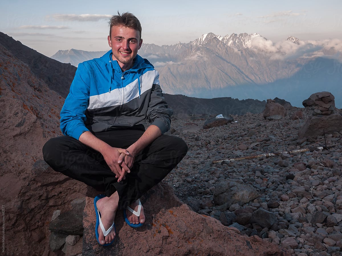 Man with flip flops sitting on a rock with snowy mountains in the background