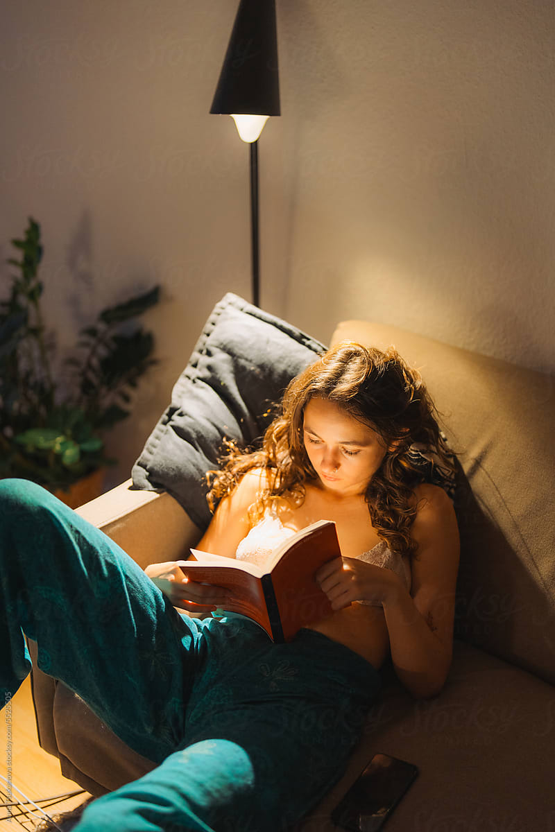 Woman laying on the couch reading book in the evening