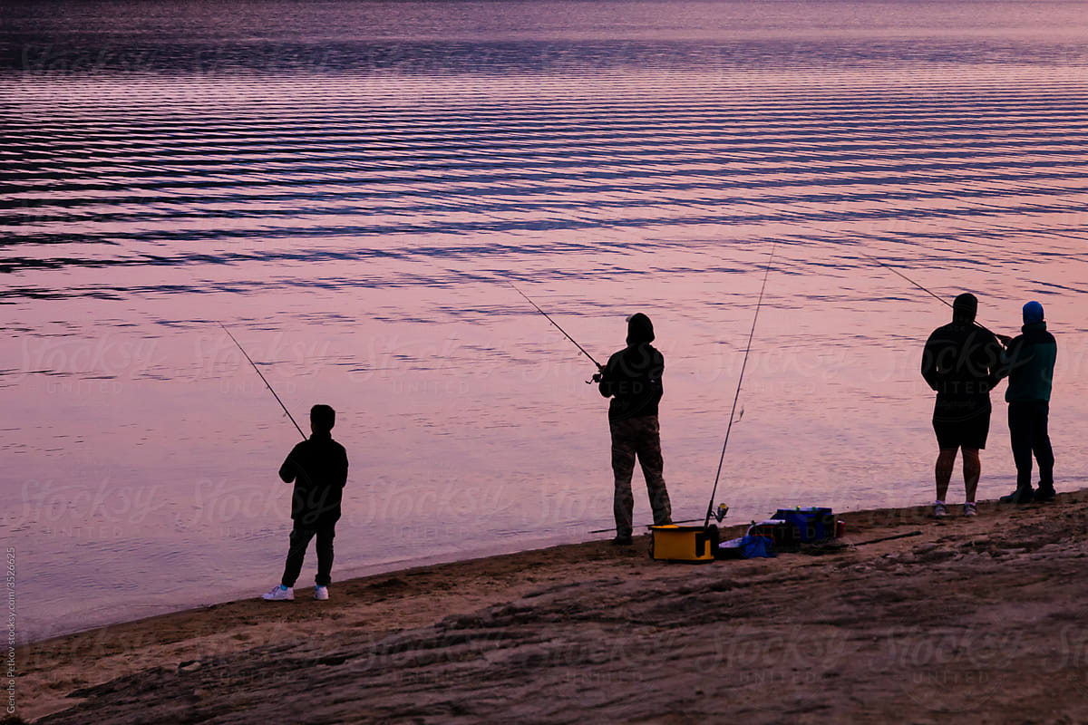 several fishermen with fishing rods on the shore of a lake catch fish, silhouette view, before Kovid 19