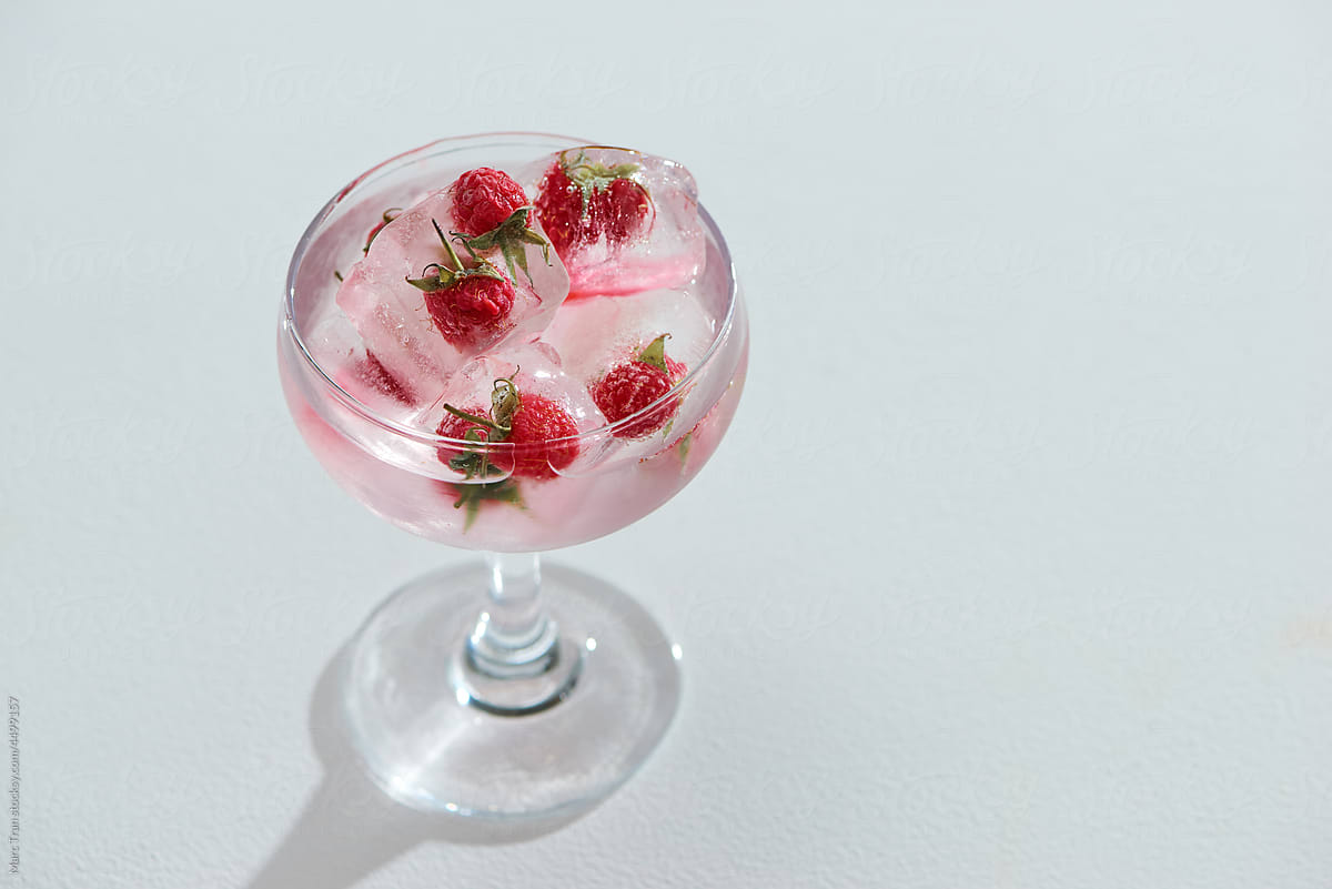 Sparkling water with berry ice cubes on white background