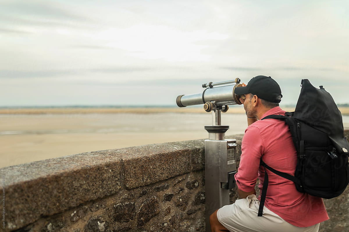 young tourist man looking at the calm sea landscape with a telescope