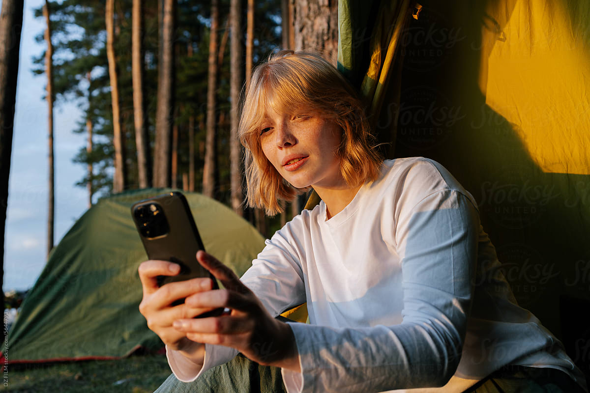 A woman uses a mobile phone sitting in a camping