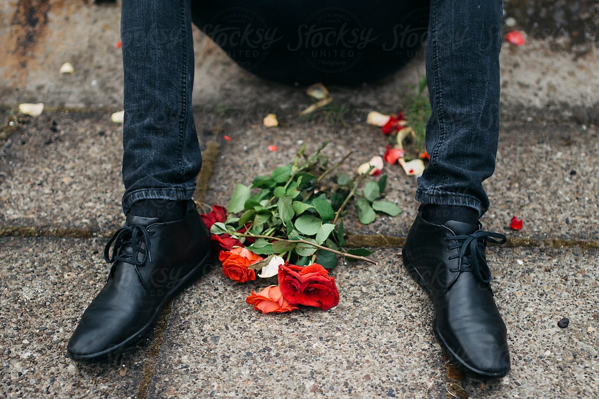 disappointment,fashionable young man sitting on the sidewalk, crushed roses