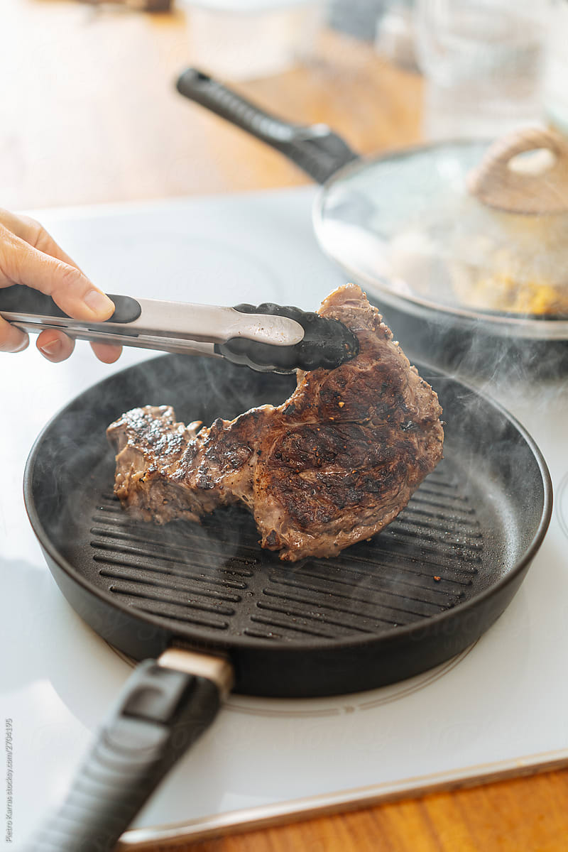 Person flipping steak with tongs on pan