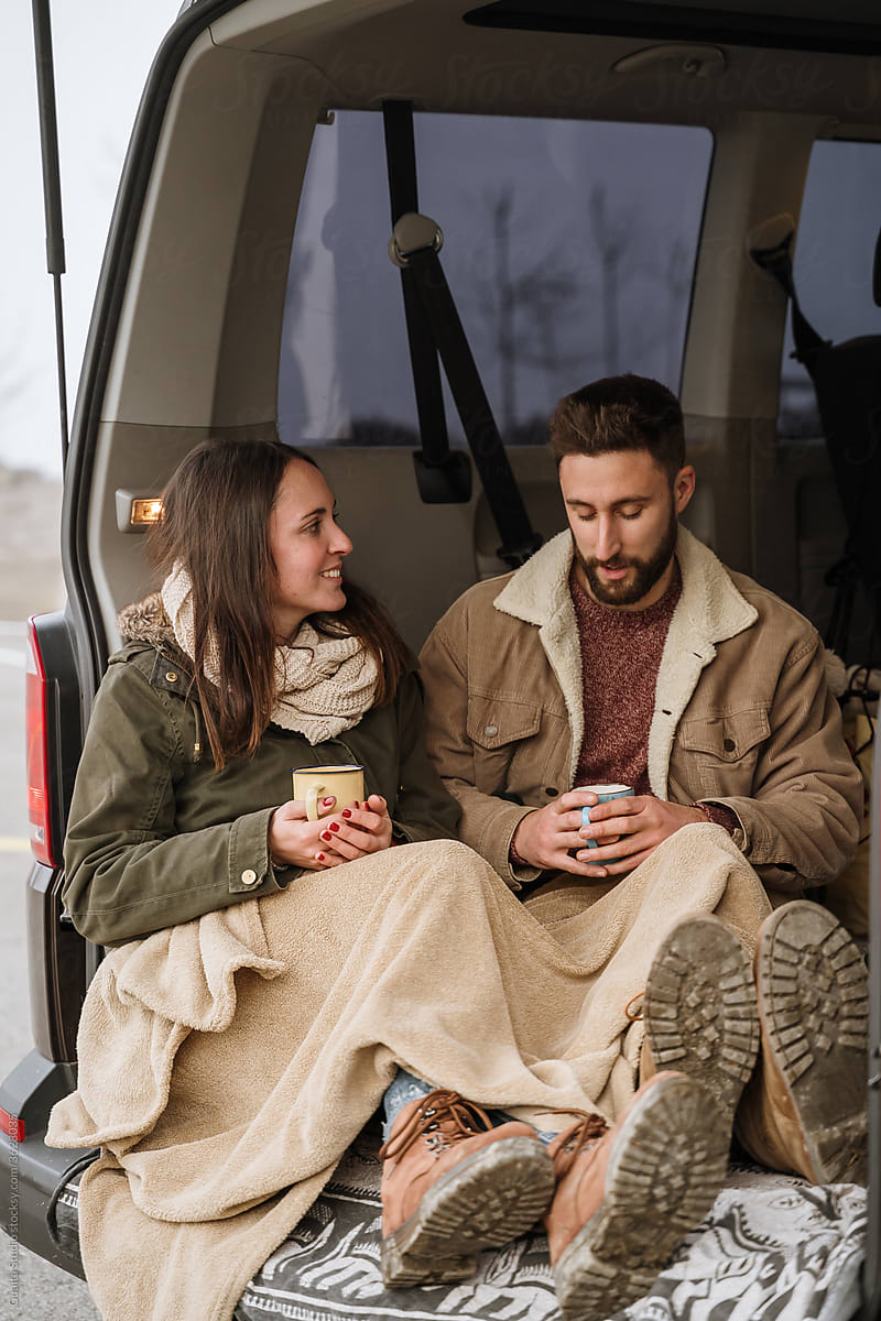 Young couple in a camper van in nature during winter having warm coffe