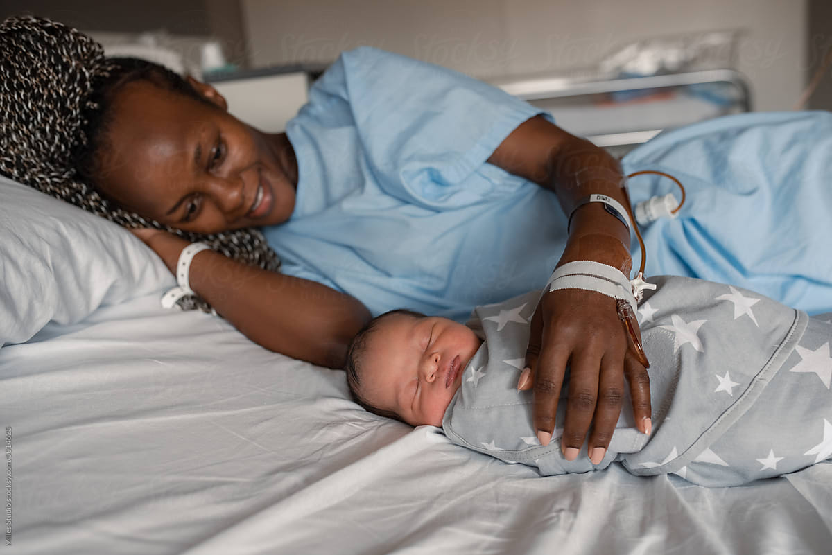African mother with infant lying on bed in ward